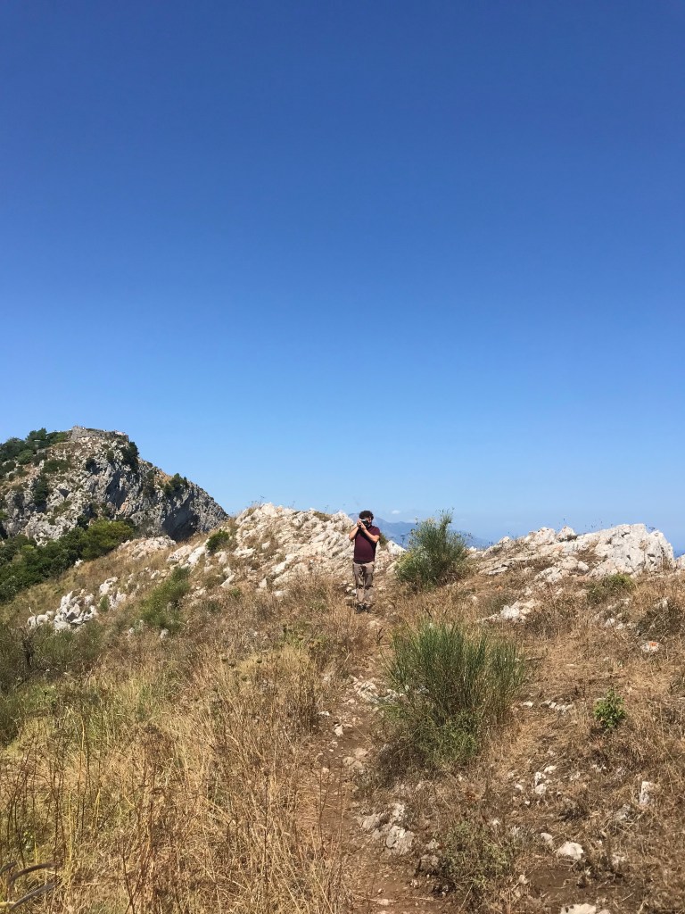 man in a field on top of a mountain with the sea as the background